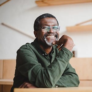 An older man wearing a green shirt and glasses smiles after receiving his dental implants