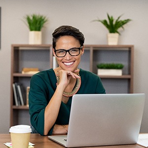 A woman sitting behind her laptop and smiling after receiving her new dental implants