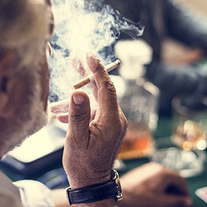 An older man wearing a leather watch and smoking a cigarette