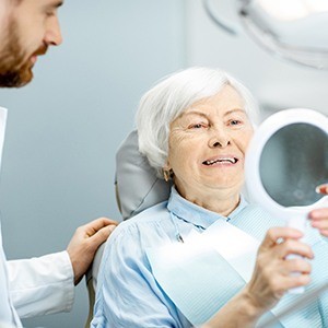 An older woman looks at her new smile while listening to her dentist explain how to maintain her new dental implants
