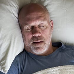 Man sleeping soundly in bed thanks to sleep apnea therapy