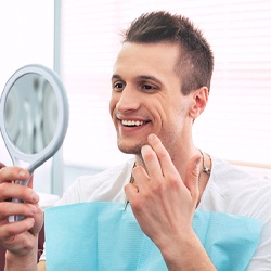 Man admiring smile in mirror after teeth whitening in Fairfax, VA