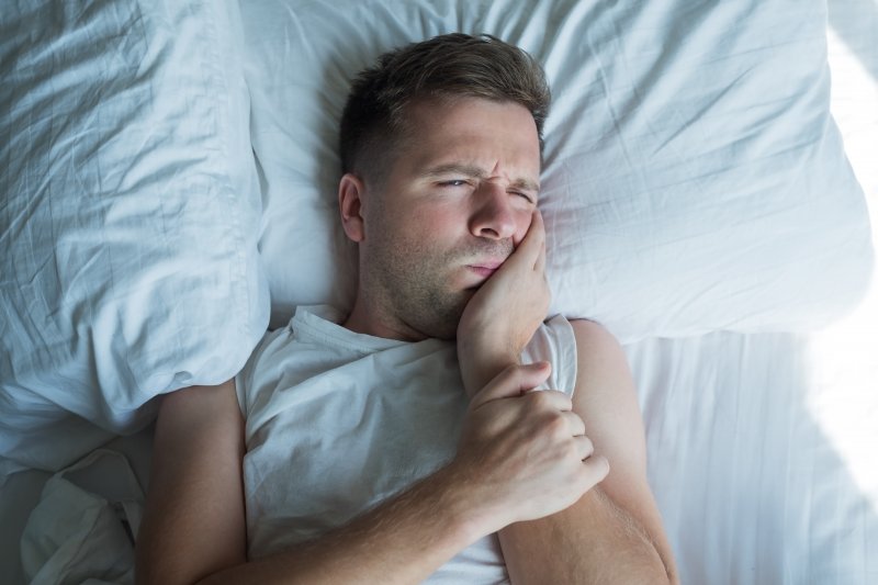 Person lying in bed holding their tooth in pain