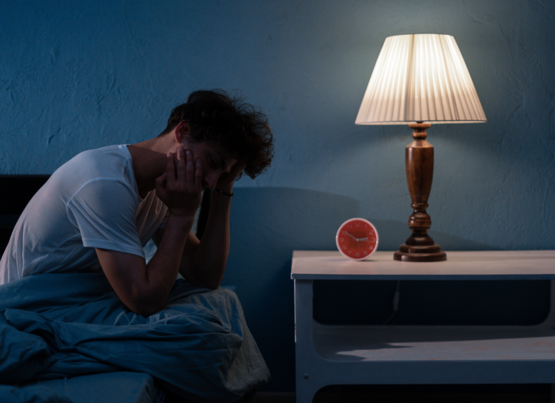 Man sitting on edge of bed holding head in hands