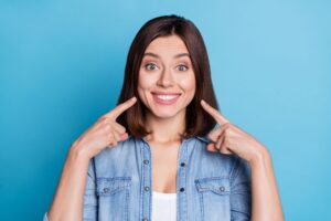 Woman wearing denim pointing to her smile with both pointers