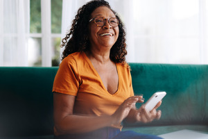 Senior woman sitting on couch while using smartphone
